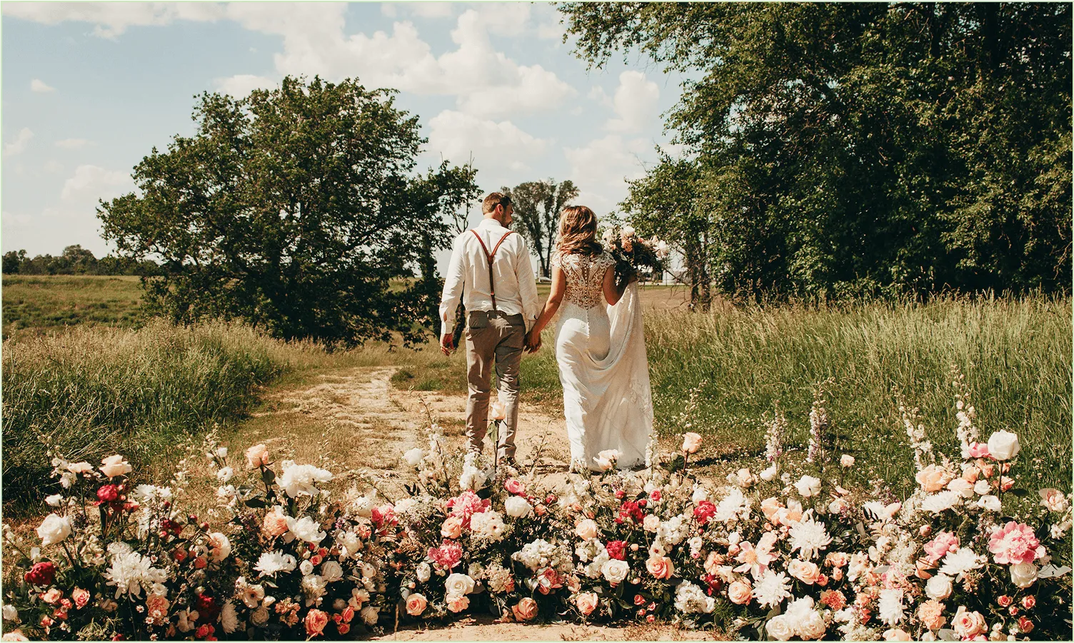 A couple walking hand in hand down a country path lined with wildflowers